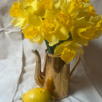 Yellow flowers in a gold vase with a lemon on a white fabric background